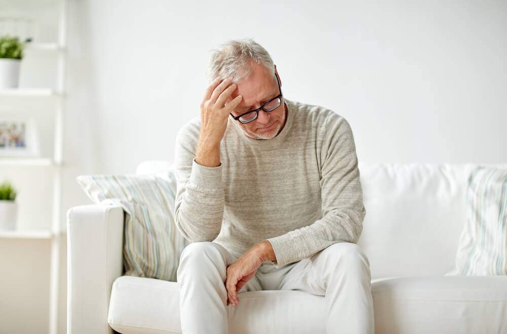 A man in his middle age is sitting on a sofa with his hand on his forehead
